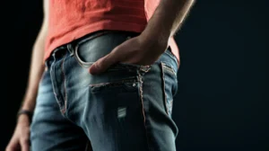 Homem de jeans com bolso aberto sobre fundo escuro em outlet de roupas.