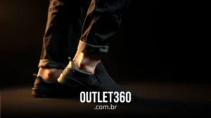 Uma pessoa usando tênis slip-on preto e calça jeans preta com punhos, em pé sobre uma superfície escura com o texto "OUTLET360.com.br" na parte inferior.
