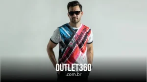 Homem usando óculos escuros pretos e uma camiseta gráfica multicolorida contra um fundo liso. O texto na parte inferior diz "OUTLET360.com.br".