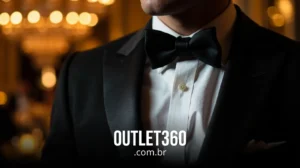 Homem de smoking preto e gravata borboleta em um evento formal, com luzes desfocadas ao fundo. O texto na parte inferior diz "OUTLET360.com.br".